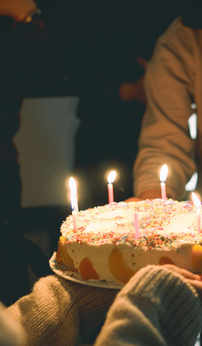 Smiling women exchanging a birthday cake with candles – DP FLOWERS BANGKOK birthday flower and gift delivery