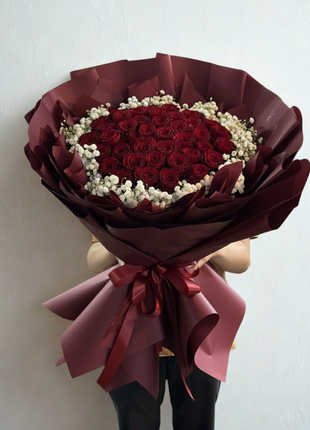 Extraordinary bouquet of 50 premium red roses arranged in dome shape with baby's breath wreath in deep red wrapping held by person - luxury Valentine's Day delivery Bangkok | DP FLOWERS BANGKOK