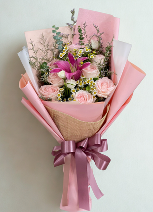 An elegant bouquet of pink roses and a large pink lily, wrapped in blush pink paper and natural fiber mesh with a mauve ribbon - Anniversary/Romantic flower delivery Bangkok | DP FLOWERS BANGKOK