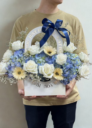 Elegant white wicker basket filled with white roses, blue hydrangeas and yellow flowers with navy ribbon - luxury flower delivery Bangkok | DP FLOWERS BANGKOK
