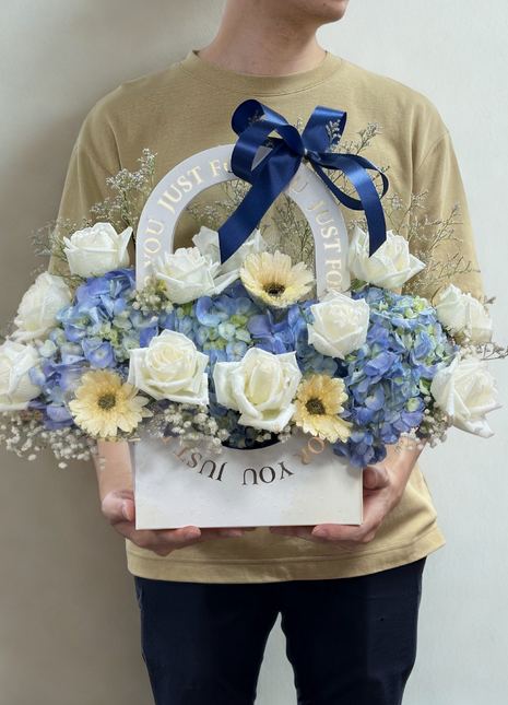 Elegant white wicker basket filled with white roses, blue hydrangeas and yellow flowers with navy ribbon - luxury flower delivery Bangkok | DP FLOWERS BANGKOK