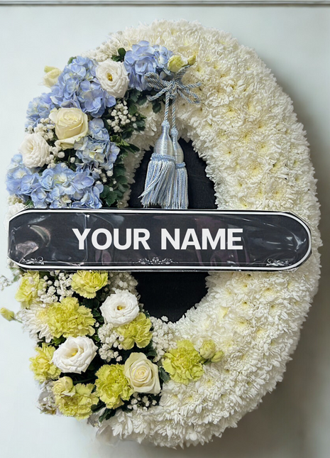 Premium condolence wreath with white chrysanthemums, blue hydrangeas, ivory roses, and yellow carnations — elegant funeral flower | DP FLOWERS BANGKOK