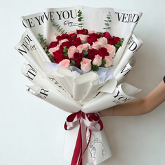 Romantic red and pink roses bouquet wrapped in artistic printed newspaper paper with burgundy ribbons and illustration tag - unique flower delivery Bangkok | DP FLOWERS BANGKOK