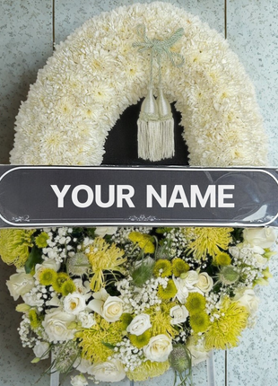 A luxurious premium funeral wreath featuring pristine white roses, lush white spray chrysanthemums, and unique green dianthus/foliage, with a central customizable banner and a decorative green tassel - funeral flower delivery Bangkok | DP FLOWERS BANGKOK