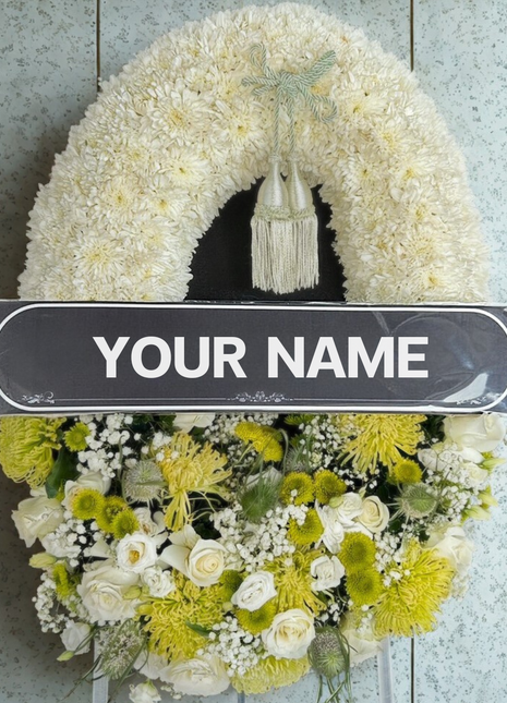 A luxurious premium funeral wreath featuring pristine white roses, lush white spray chrysanthemums, and unique green dianthus/foliage, with a central customizable banner and a decorative green tassel - funeral flower delivery Bangkok | DP FLOWERS BANGKOK