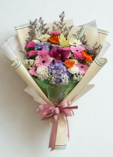 Vibrant mixed flower bouquet with pink and orange gerberas, purple hydrangeas, yellow lilies and carnations wrapped in cream paper - colorful flower delivery Bangkok | DP FLOWERS BANGKOK