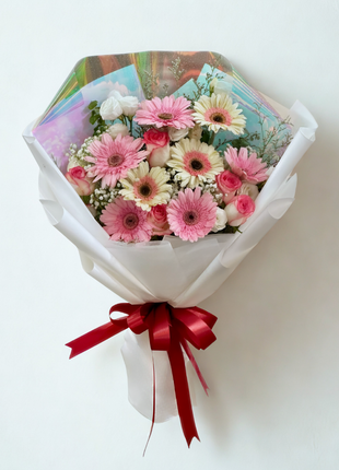 Sweet pink and cream gerbera daisy bouquet with roses wrapped in white paper with holographic accent and red ribbon - romantic flower delivery Bangkok | DP FLOWERS BANGKOK
