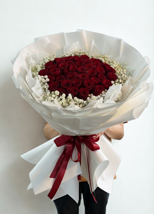 Extraordinary bouquet of 50 premium red roses arranged in dome shape with baby's breath wreath in white wrapping held by person - luxury Valentine's Day delivery Bangkok | DP FLOWERS BANGKOK