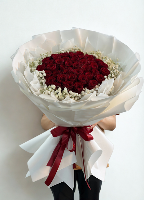 Extraordinary bouquet of 50 premium red roses arranged in dome shape with baby's breath wreath in white wrapping held by person - luxury Valentine's Day delivery Bangkok | DP FLOWERS BANGKOK
