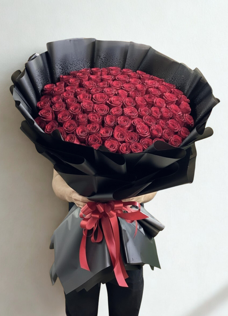 Spectacular bouquet of 100 premium red roses in massive dome arrangement with luxury black wrapping and red ribbon held by person - ultimate Valentine's Day delivery Bangkok | DP FLOWERS BANGKOK