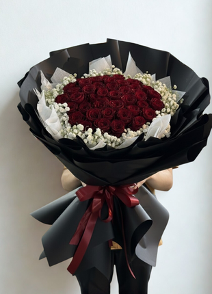 Extraordinary bouquet of 50 premium red roses arranged in dome shape with baby's breath wreath in luxury black wrapping held by person - luxury Valentine's Day delivery Bangkok | DP FLOWERS BANGKOK