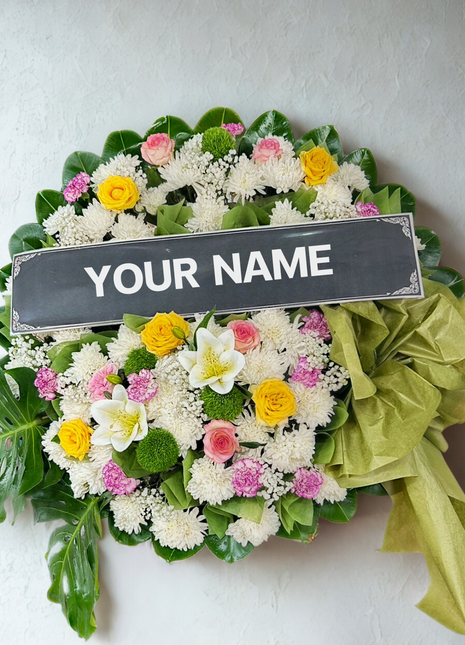 Bright colorful funeral wreath with yellow roses, pink flowers, white chrysanthemums and green ribbon with personalized nameplate - vibrant memorial delivery Bangkok | DP FLOWERS BANGKOK