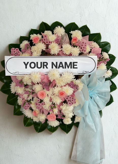 Soft pink and cream funeral wreath with roses, chrysanthemums and blue ribbon with personalized nameplate - gentle memorial delivery Bangkok | DP FLOWERS BANGKOK