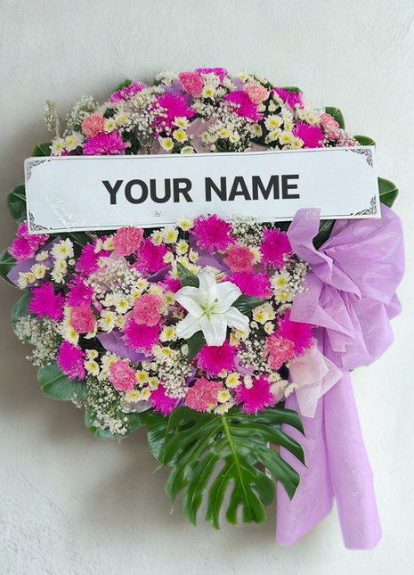 Bold pink and white funeral wreath with fuchsia chrysanthemums, white lily and purple ribbon with personalized nameplate - vibrant memorial delivery Bangkok | DP FLOWERS BANGKOK