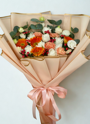 An elegant bouquet of white roses, orange gerbera, and coral carnations, wrapped in peach paper with a gold border and matching ribbon - Housewarming/Luxury flower delivery Bangkok | DP FLOWERS BANGKOK