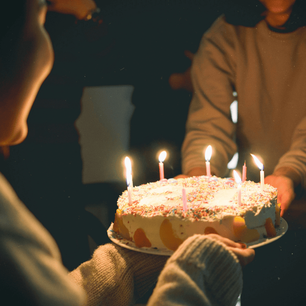 Smiling women exchanging a birthday cake with candles – DP FLOWERS BANGKOK birthday flower and gift delivery